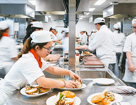 Cooks in training preparing food in an industrial kitchen.
