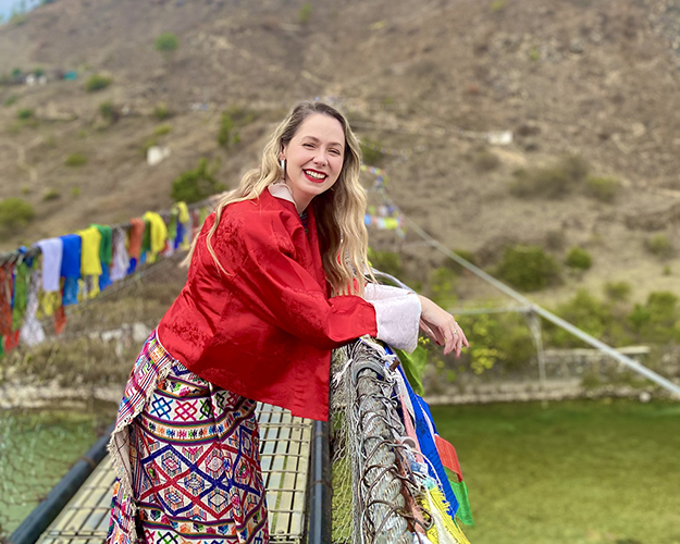 Samantha standing on a footbridge adorned with colourful Buddhist flags