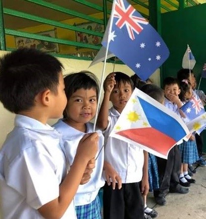 Children waving Australian and Philippine flags during a visit to an elementary school supported by our classroom construction program