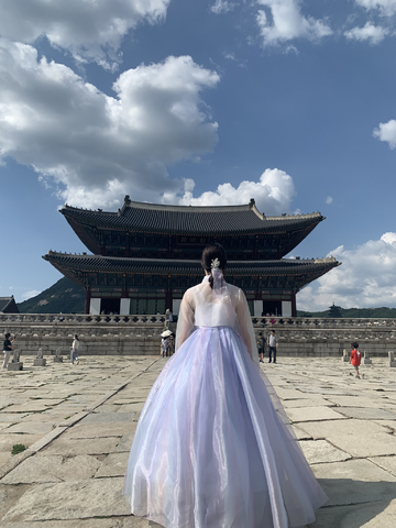 Photo of Seana with back to camera looking at a historic Gyeonbok Palace, wearing a big puffy purple dress.
