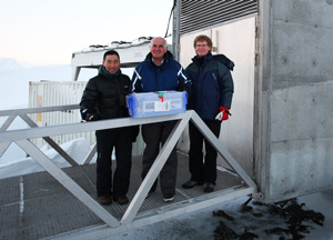 Three people standing at concrete entrance to vault, holding a sealed box