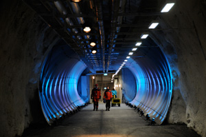 Two people walking in large tunnel lit by blue light