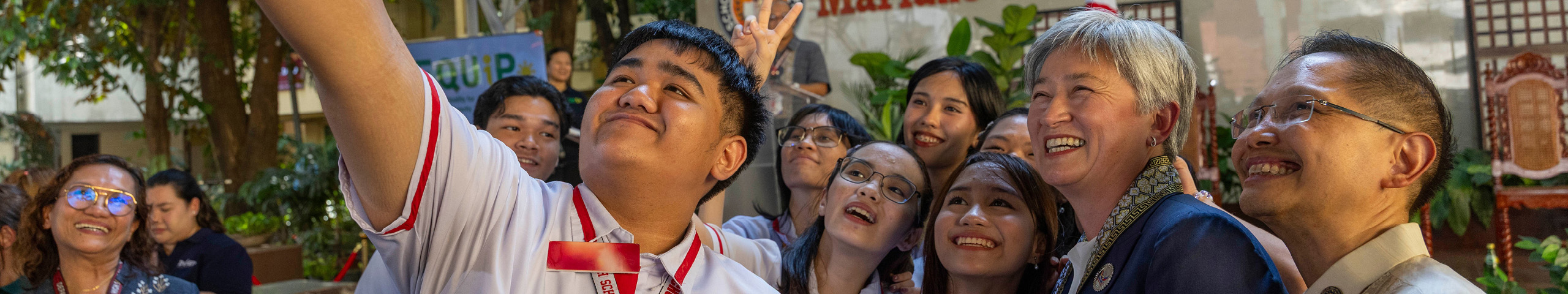 Students gather for a group selfie outside a school building during a community event with Minister Penny Wong..