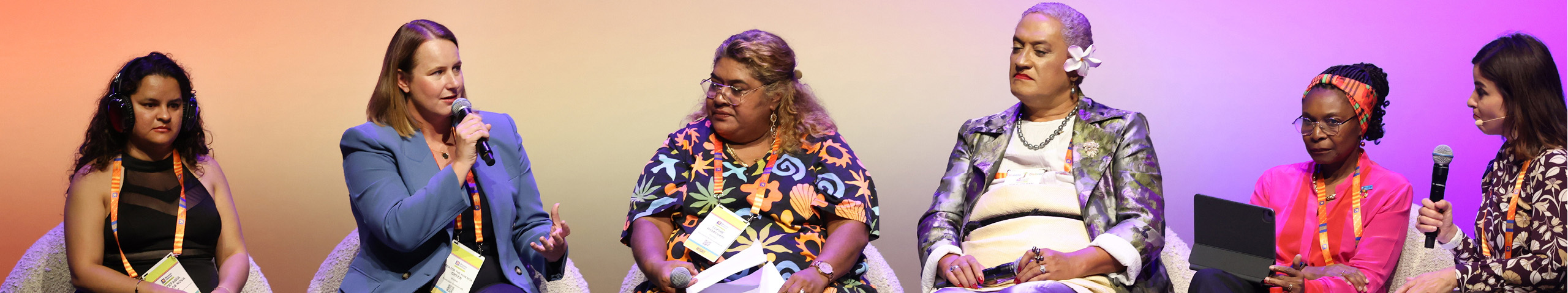 Panel speakers participate in a conference discussion on stage, seated in front of an audience during a formal event.