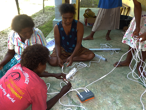 Ladies working with cords plugged into unit on the floor, learning about solar technologies