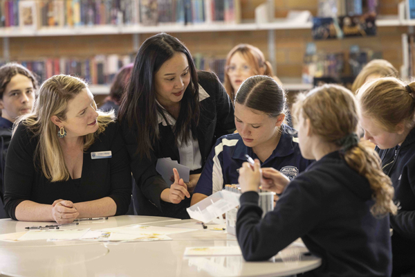 Teacher and facilitator support students working together on a classroom activity at a round table.