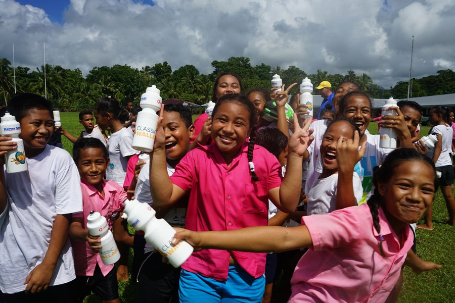Group photo of many kids, holding water bottles, playing on a field. 