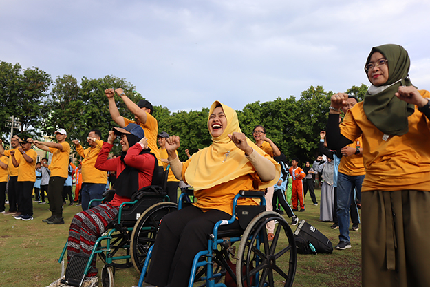 Group of excited Indonesian people, in wheelchairs, outdoors, pumping their fists in the air.