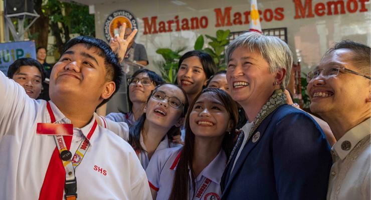 Students gather for a group selfie outside a school building during a community event with Foreign Minister Penny Wong.