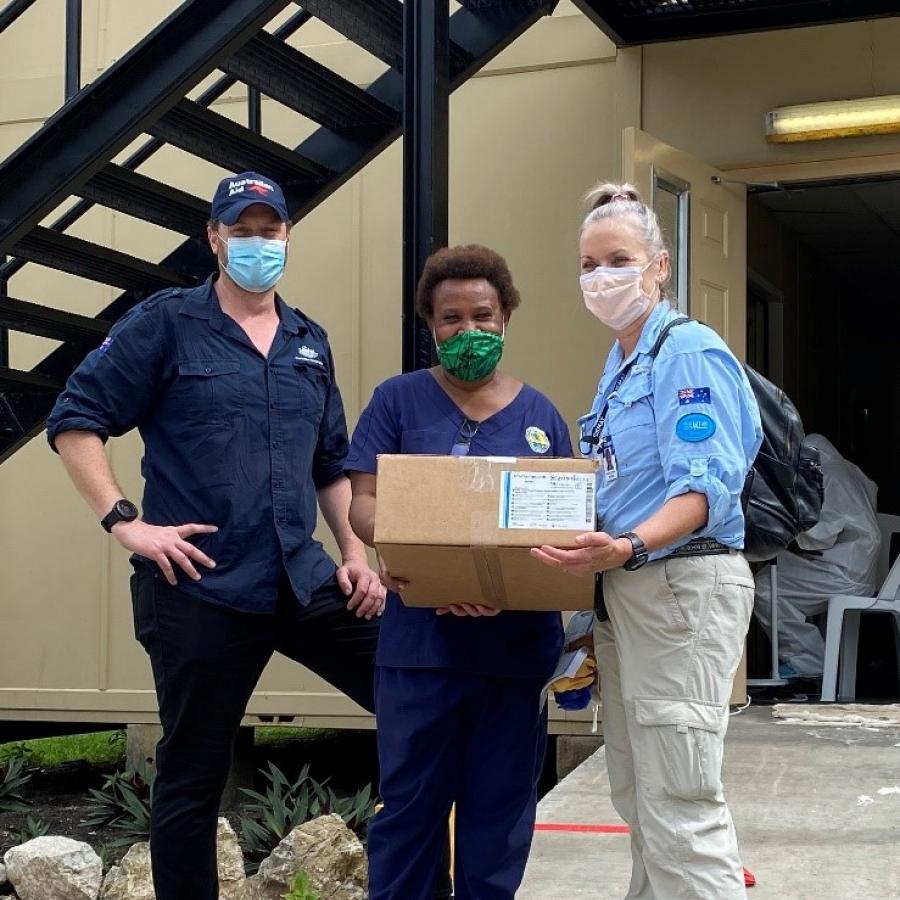 Two Australian medical specialists stand next to a Papua New Guinea frontline worker, presenting a box that contains an inline suction device for the Port Moresby General Hospital.