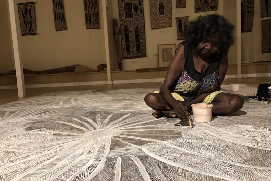 An indigenous artist, sitting on the ground working on a line drawing