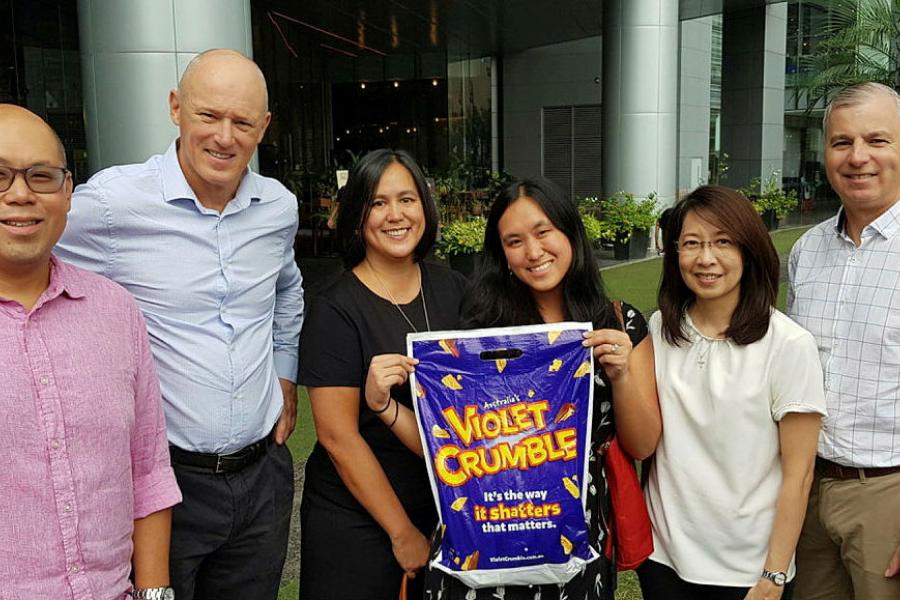 Group of six people, three men, three women standing in front of building.  Two women in centre are holding a purple violent crumble  show bag. Names and positions of people included in photo caption. 