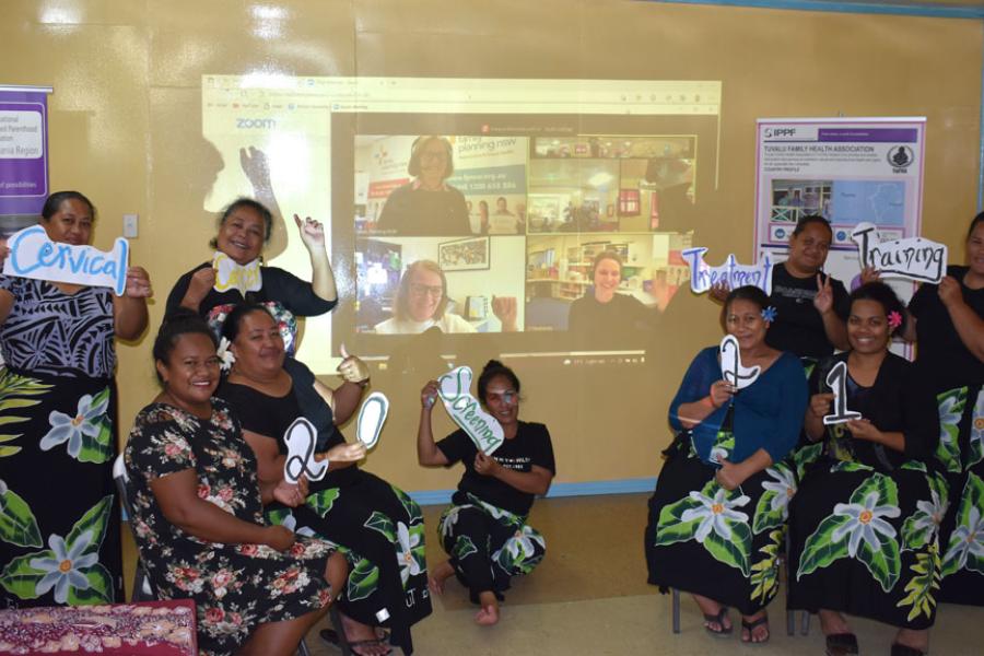 Group of 9 women holding signs saying "cervical cancer treatment training 2021" and the reflection of a zoom call showing others participants.