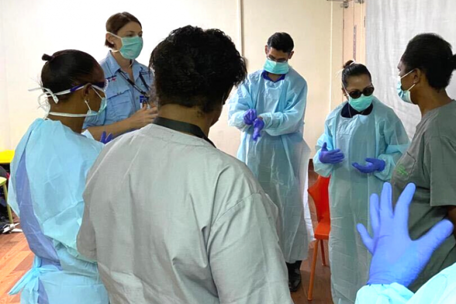 A group of medical specialists from Australia and Papua New Guinea gather in a circle, wearing protection equipment.