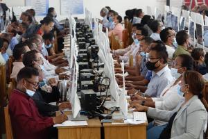 Rows of Timorese civil servants, seated closely together and wearing masks, intently focused on taking a computerised test as part of the civil service promotion process.