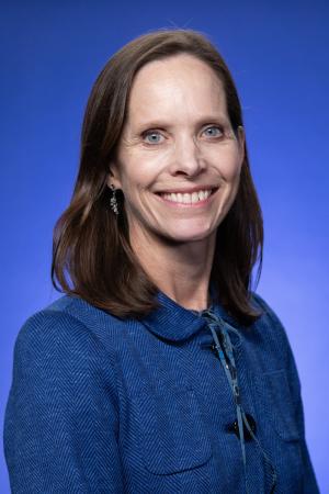 Headshot of Fiona, wearing a royal blue buttoned shirt, with a smiling expression