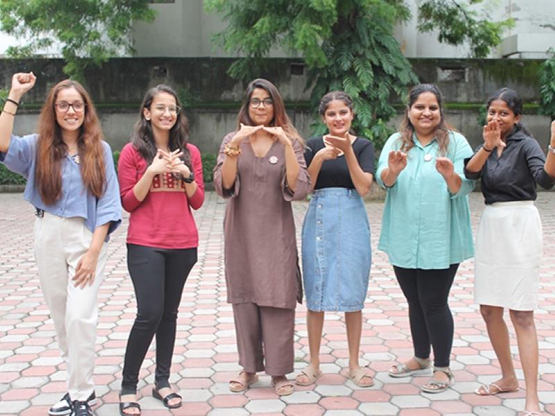 six women standing together making signs with their hands.