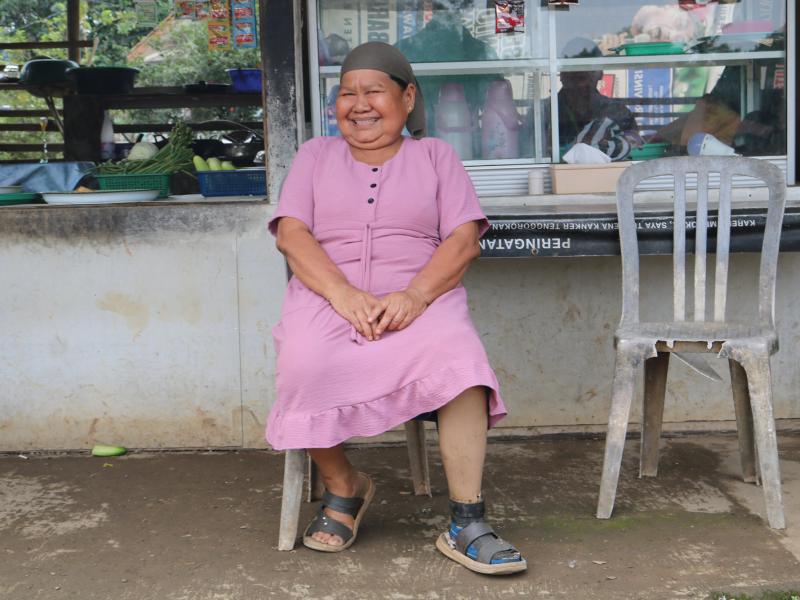 Female with a prosthetic leg, smiling and sitting on a chair in front of a food stall