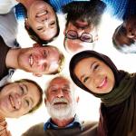 Group of diverse people gathered around in a circle looking down at photographer.