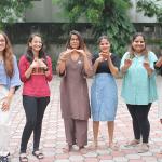 six women standing together making signs with their hands.