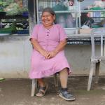 Female with a prosthetic leg, smiling and sitting on a chair in front of a food stall