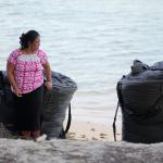 A female standing in front two large sandbags on a beach.