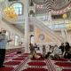 Group of people seated on a carpet listening to a religious leader speaking in a mosque.