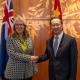 Jan Adams and Ma Zhaoxu shaking hands in front of the flags of Australia and China.