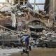 A man wearing a mask walks through the streets of Beirut, with damaged buildings and cars in the background.