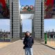 Person standing in front of large sculptural entrance and Olympic rings logo 