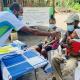 Community Health Worker doing a temperature check on a baby sitting in the fathers lap. 