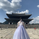 Photo of Seana with back to camera looking at a historic Gyeonbok Palace, wearing a big puffy purple dress.