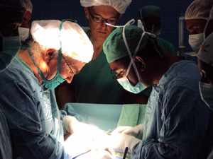 Photo of two surgeons operating, with a doctor in the background