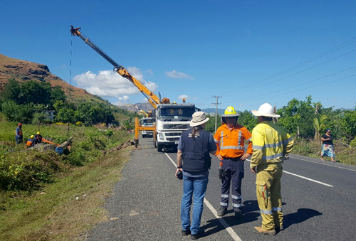 Three people standing in front of a truck which is repairing fallen electricity poles