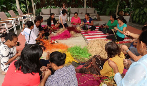 Women in a cricle around brightly coloured grass, weaving.