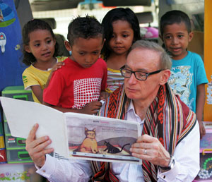 Four young children gather around Mr Carr while he reads them a story about cats
