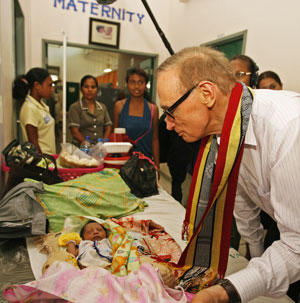 Senator Carr leans looks tenderly at a tiny baby in a maternity ward