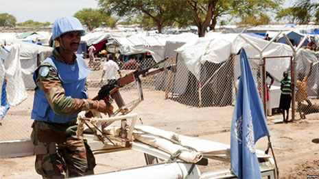 Peacekeeper holding a gun, tent city in background