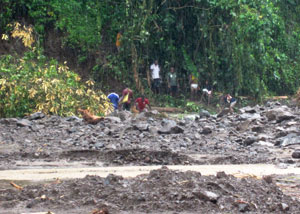 A group of people standing on the bank of a flooded and debris filled river