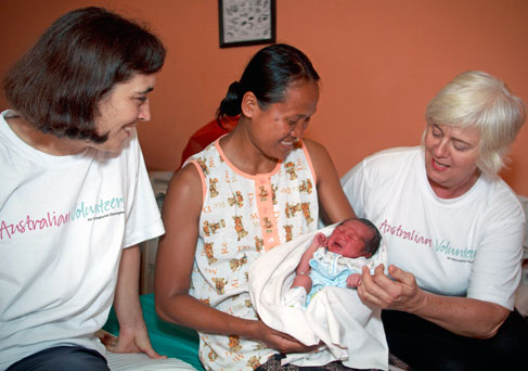 Three women sitting on a bed, the middle one holding a newborn baby