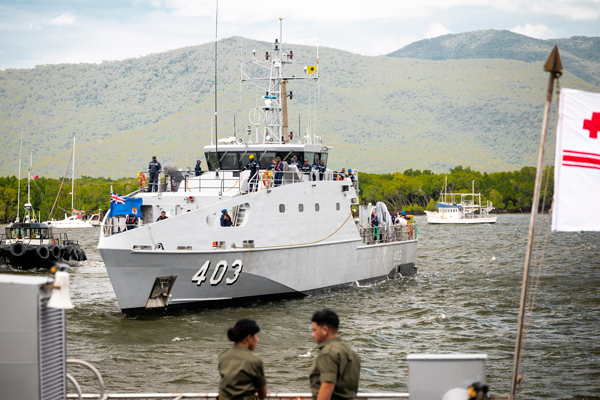 Patrol boat number 403 travelling through a harbour, with crew on deck and green hills in the background.