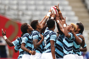 Women rugby players in blue striped uniforms reaching together for the ball during a match.