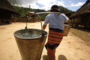 Woman carrying buckets of water using a timber pole across her shoulder