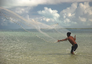 Man in shorts standing in shallow, calm ocean water throwing a large fishing net