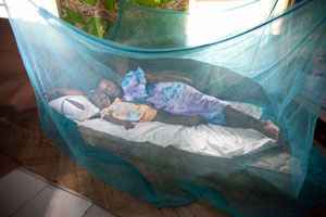 A mother and child pretend to sleep under a Long Lasting Insecticide treated Net