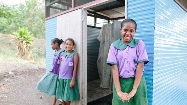 Three girls in school uniform standing outside a toilet in their local school. 