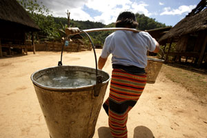 A woman carrying large containers of water across her shoulders
