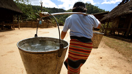 Woman carrying large buckets of water through a village