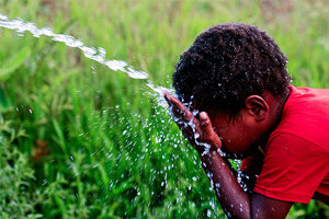 Photo of a young boy washing his face under a spout of clean water