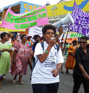 Women marching along a street holding banners and using a megaphone